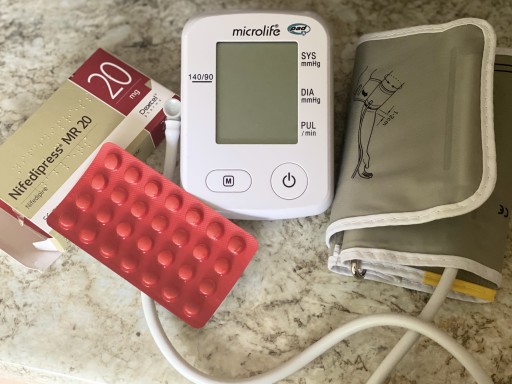 Blood pressure monitor alongside medication lying on a marble surface.